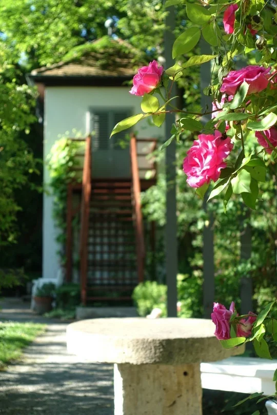Ein runder Steintisch, dahinter ein kleiner Turm in einem sommerlichen Garten